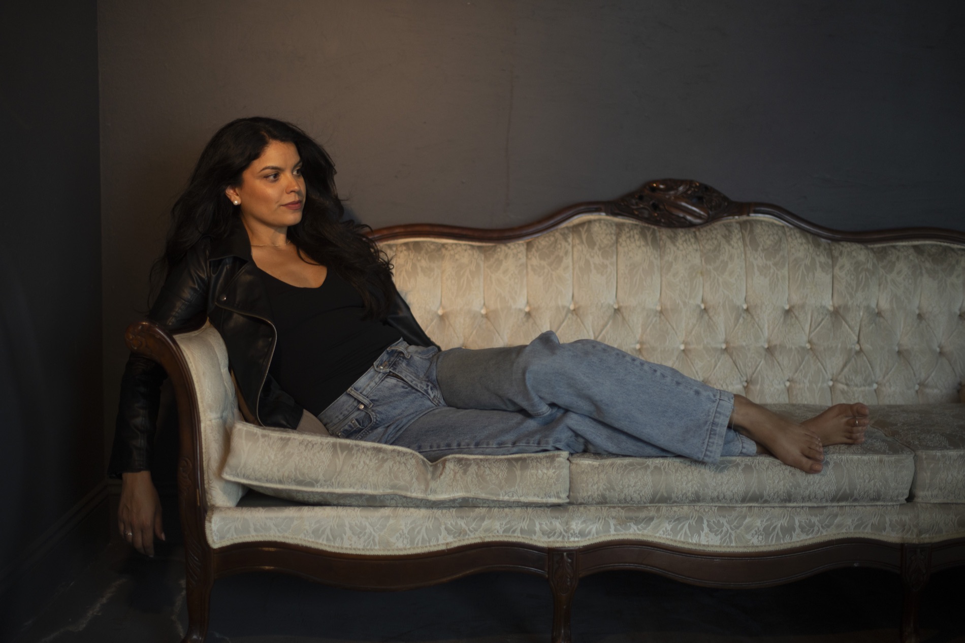 Kimberly reclining on a vintage sofa in a dark editorial scene