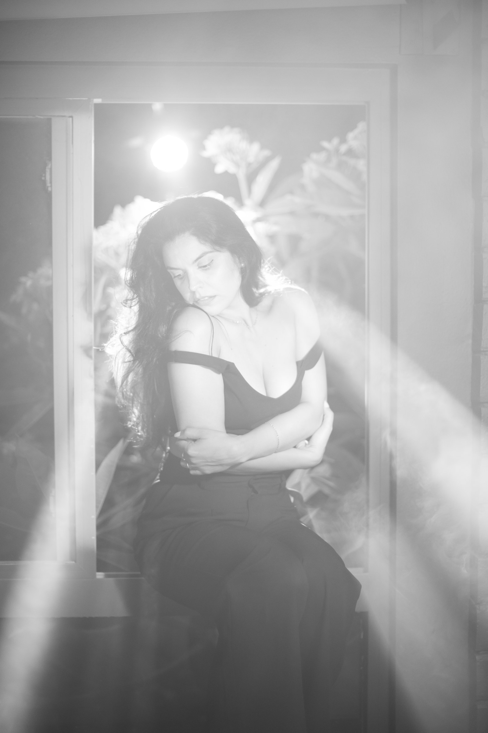 Black and white self-embrace portrait of Kimberly by a window in misty light